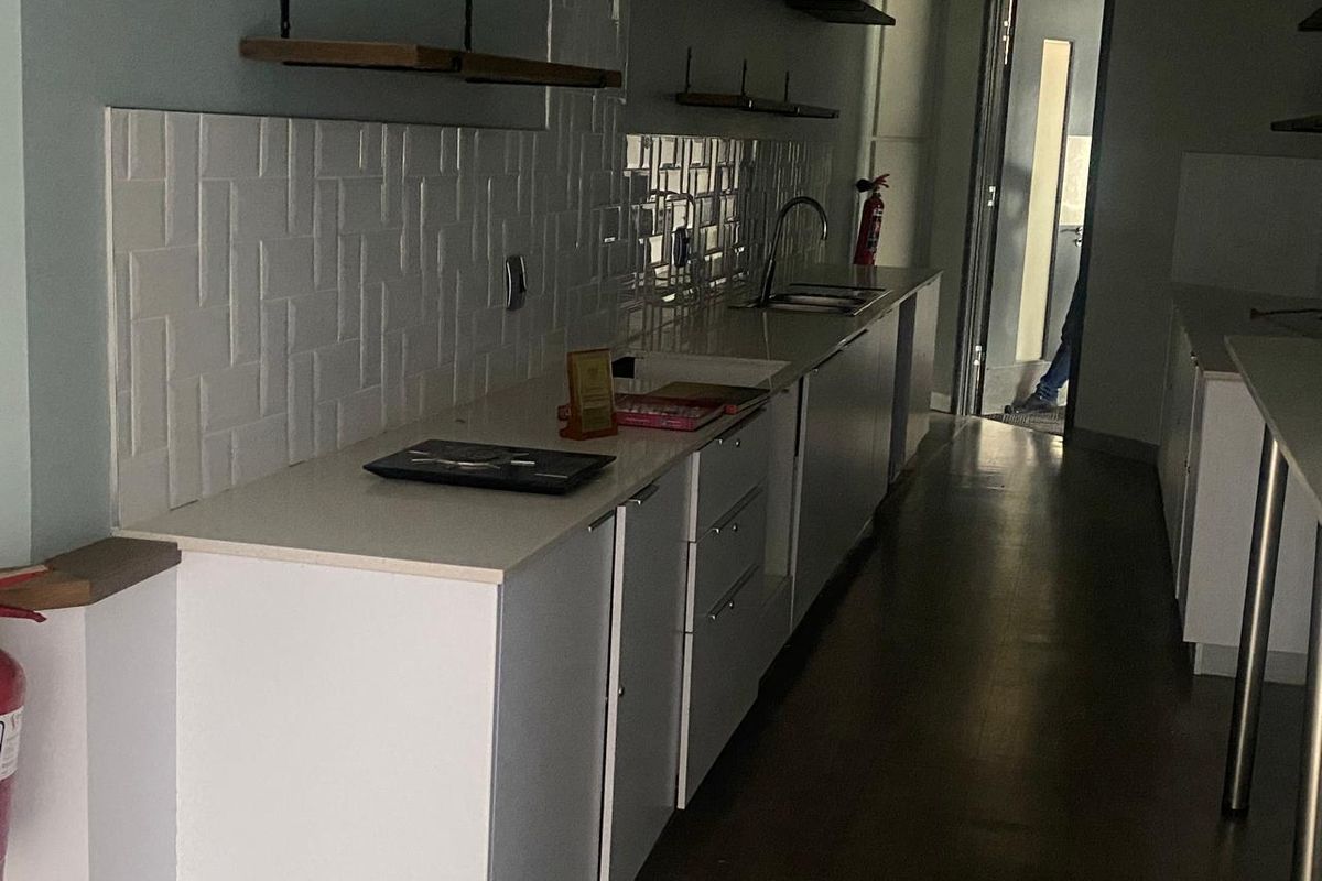 A modern office kitchenette featuring white cabinetry, quartz countertops, a subway tile backsplash, and floating shelving.