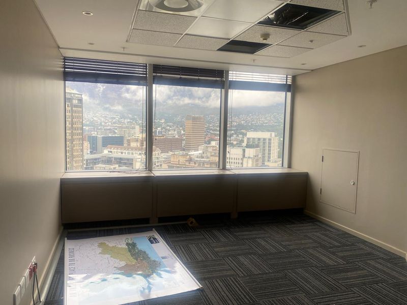 Empty office space featuring carpet tiles, a suspended ceiling, and large windows offering expansive city views.