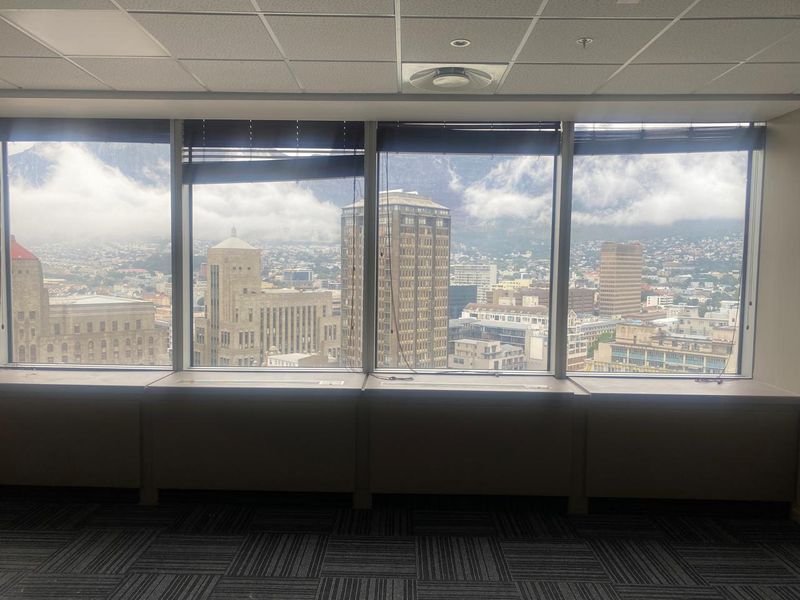 Empty office space featuring large floor-to-ceiling windows with expansive city and mountain views, suspended ceiling, and carpeted flooring.