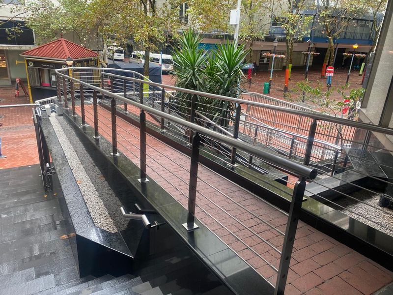 An accessible paved ramp entrance featuring modern stainless steel handrails and stone detailing, providing a clean and professional approach to the office building.