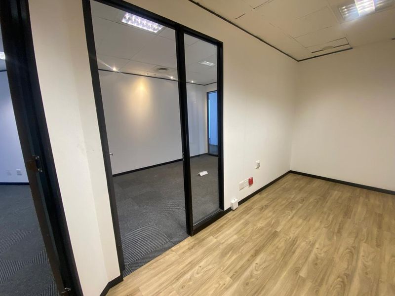 Empty office space featuring a glass partition, wood-look vinyl flooring, carpeted interior area, and suspended ceiling with recessed lighting.