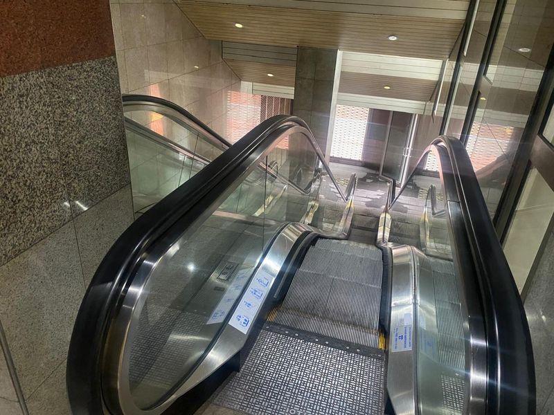 A modern office building interior featuring a functional escalator with glass balustrades and polished granite wall finishes.