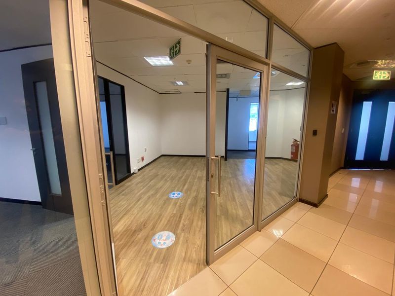 A vacant office space featuring glass partition walls, aluminum framing, suspended ceilings, and wood-look flooring, suitable for a professional workspace.