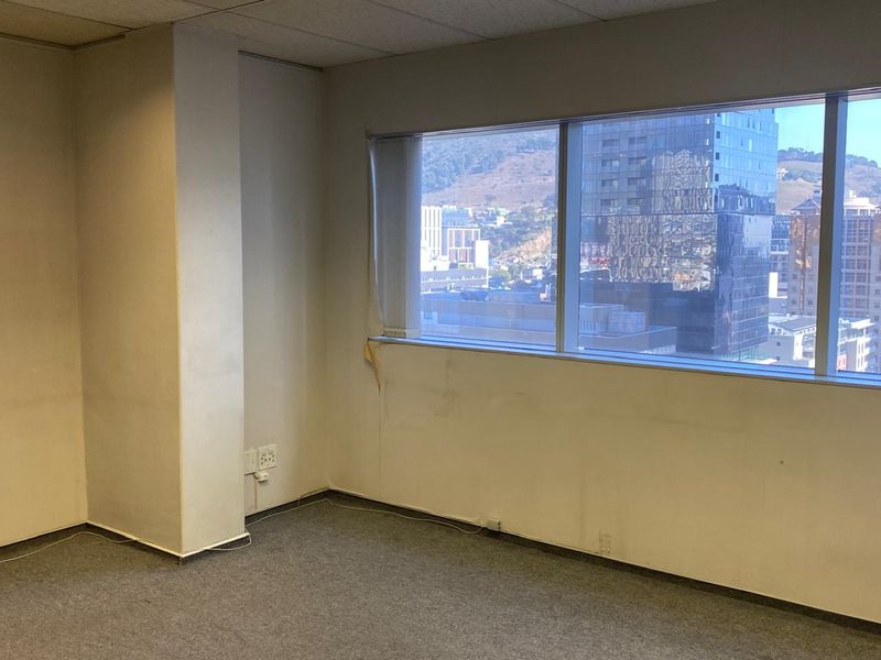 An empty office space featuring a large window with city views, carpeted flooring, and a suspended ceiling, ready for customization.