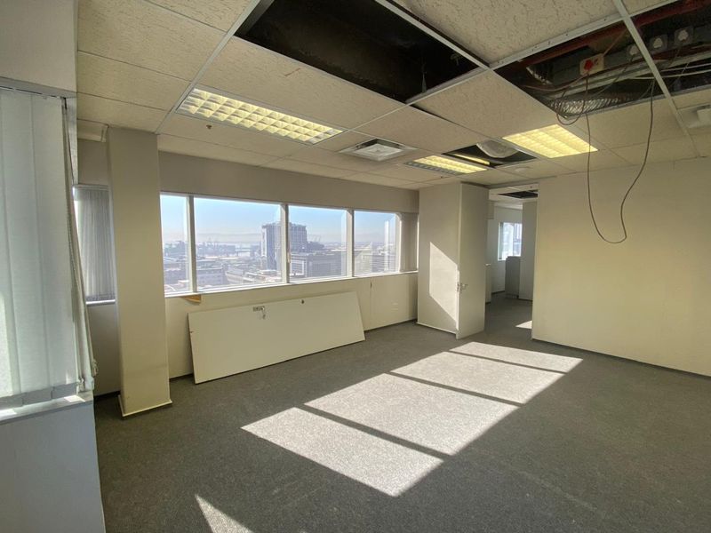 An empty office space featuring large windows with city views, carpeted flooring, and a suspended ceiling requiring maintenance and repair.