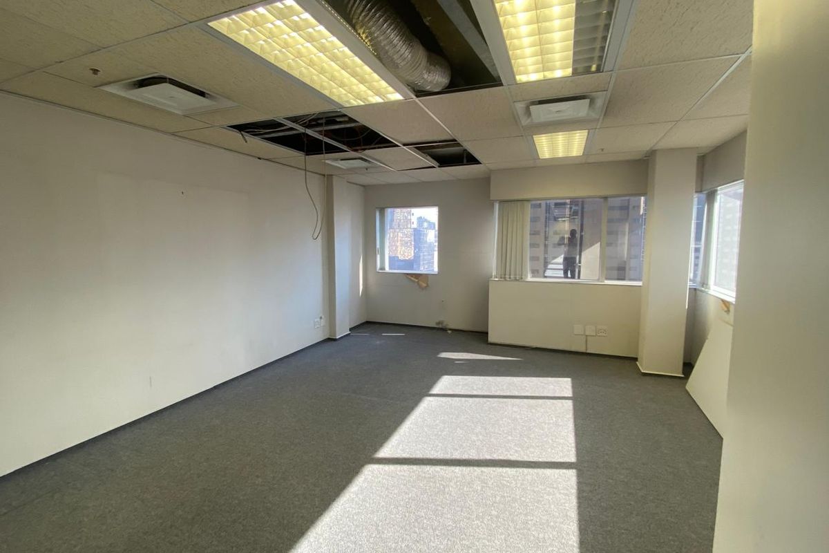 An empty office space featuring large windows, carpeted flooring, and a suspended ceiling with visible maintenance requirements.