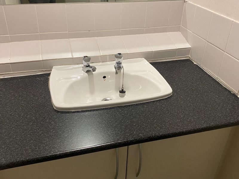 A functional bathroom vanity area featuring a white basin, dark laminate countertop, and tiled splashback.