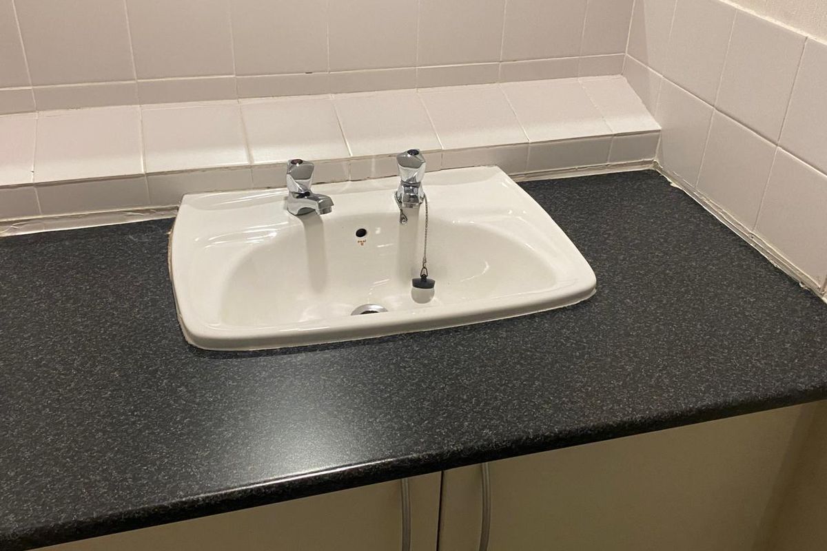 A functional bathroom vanity area featuring a white basin, dark laminate countertop, and tiled splashback.