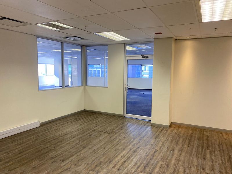 A bright, vacant office space featuring modern laminate flooring, a suspended ceiling with recessed lighting, and glass partitions providing an open, professional atmosphere.