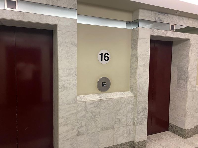 A clean and professional office building elevator lobby featuring marble wall cladding and dual elevator access on the sixteenth floor.