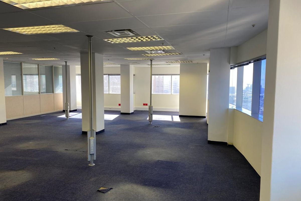 Spacious open-plan office area featuring large windows, suspended ceilings with recessed lighting, and carpeted flooring throughout.