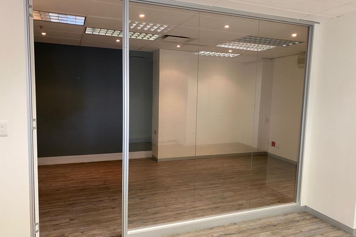 A modern, empty office space featuring a glass partition wall, recessed lighting, and wood-look laminate flooring, suitable for a professional workspace.