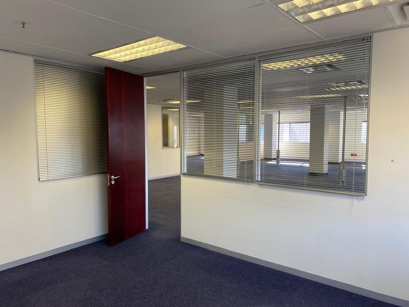 An empty office space featuring carpet flooring, suspended ceilings with recessed lighting, and internal glass partitioning with integrated venetian blinds.