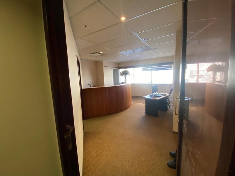 A functional office space featuring a built-in reception desk, suspended ceiling with recessed lighting, and large windows providing natural light.