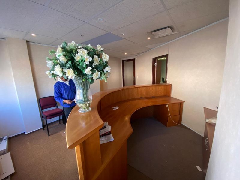 Office reception area featuring a large built-in wooden desk, suspended ceiling with recessed lighting, and carpeted flooring.