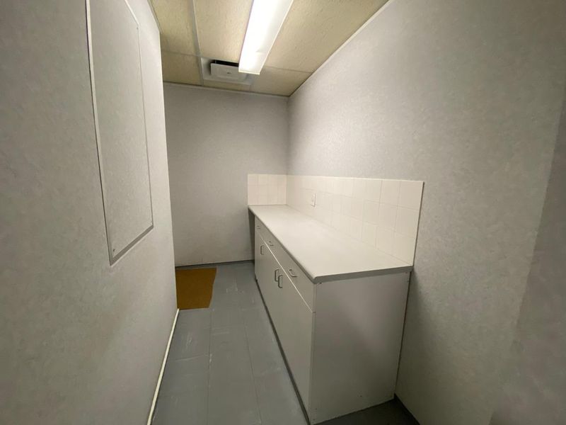 A functional utility or scullery area featuring built-in cabinetry, a laminate countertop, and tiled splashback, suitable for office storage or prep.
