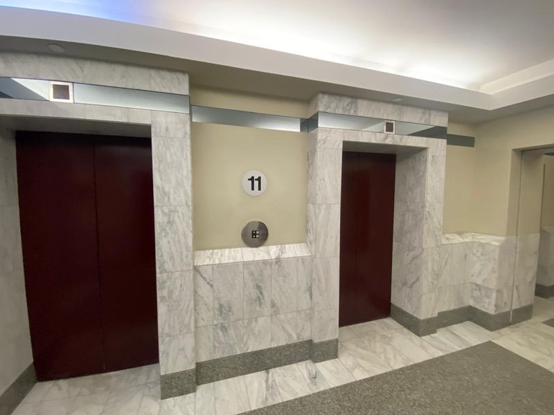 A well-maintained office building elevator lobby featuring marble wall cladding, marble flooring, and dual elevator access on the eleventh floor.