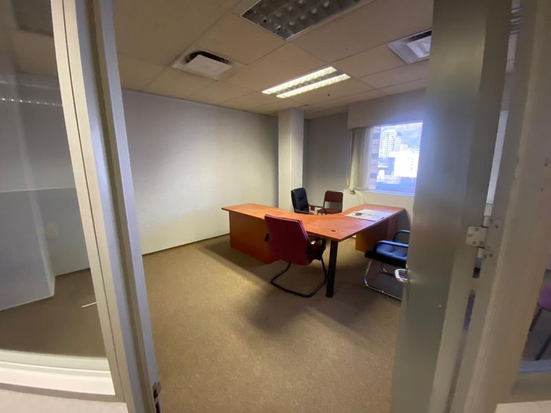 A functional office space featuring carpeted flooring, a suspended ceiling with recessed lighting, and a glass partition wall.