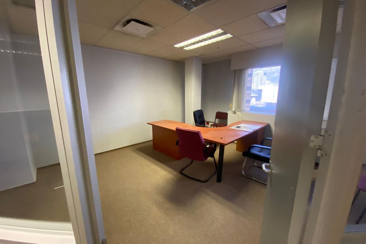 A functional office space featuring carpeted flooring, a suspended ceiling with recessed lighting, and a glass partition wall.