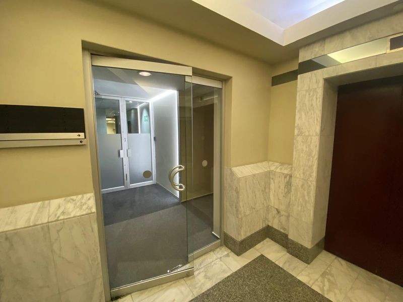 A professional office building entry lobby featuring marble wall cladding, marble flooring, and a modern glass pivot door leading to the elevator area.