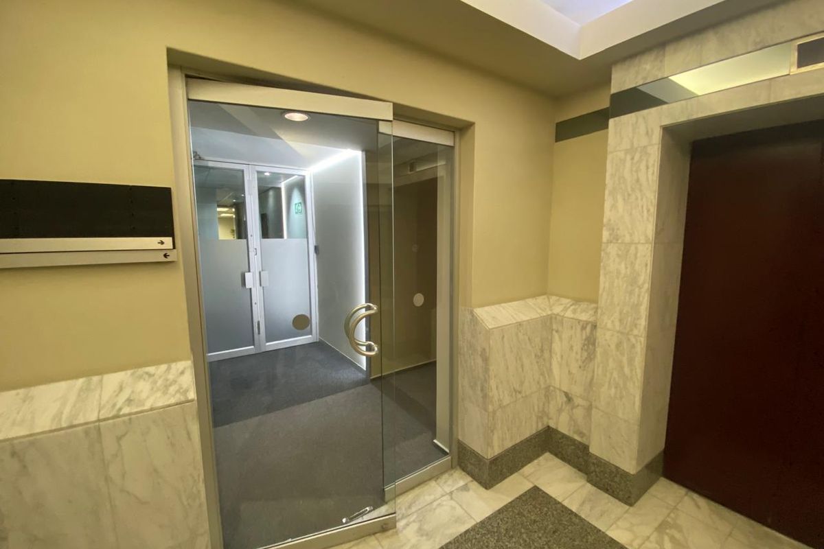 A professional office building entry lobby featuring marble wall cladding, marble flooring, and a modern glass pivot door leading to the elevator area.