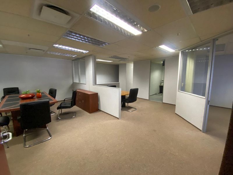 Open-plan office space featuring glass partitions, suspended ceilings with integrated lighting, and carpeted flooring, suitable for a professional work environment.