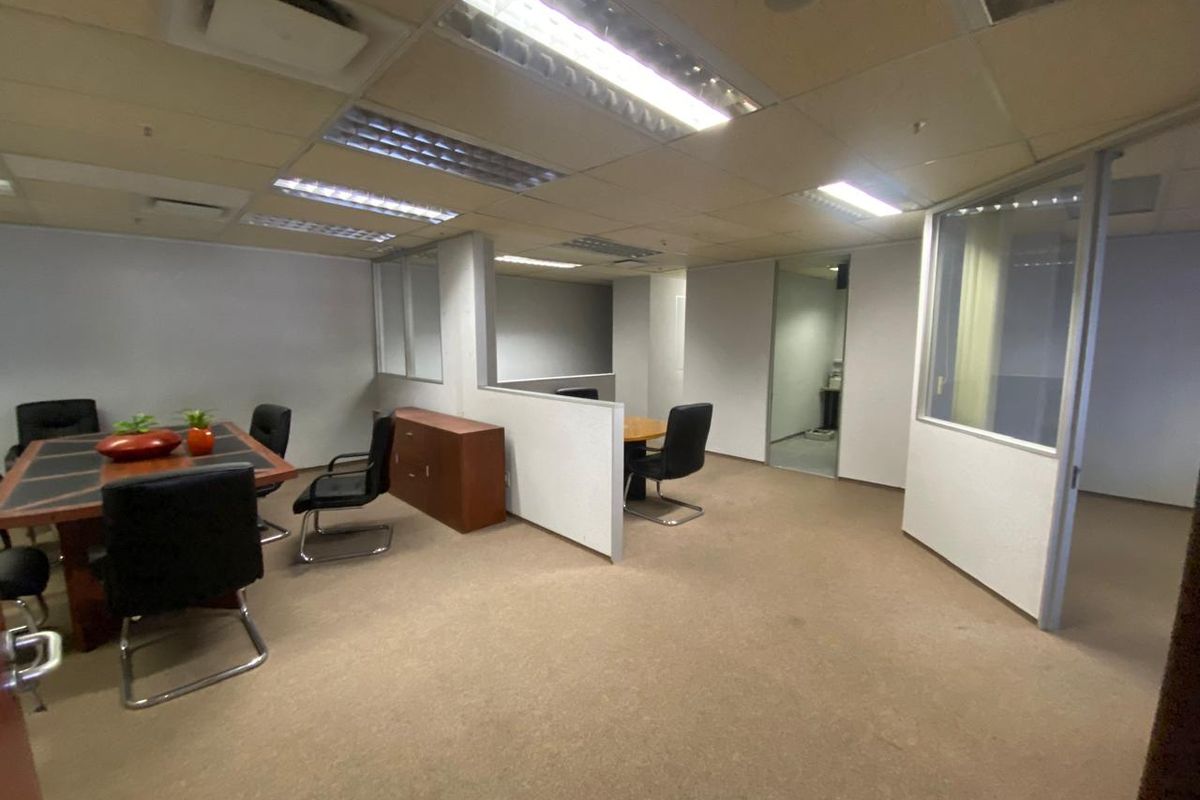 Open-plan office space featuring glass partitions, suspended ceilings with integrated lighting, and carpeted flooring, suitable for a professional work environment.