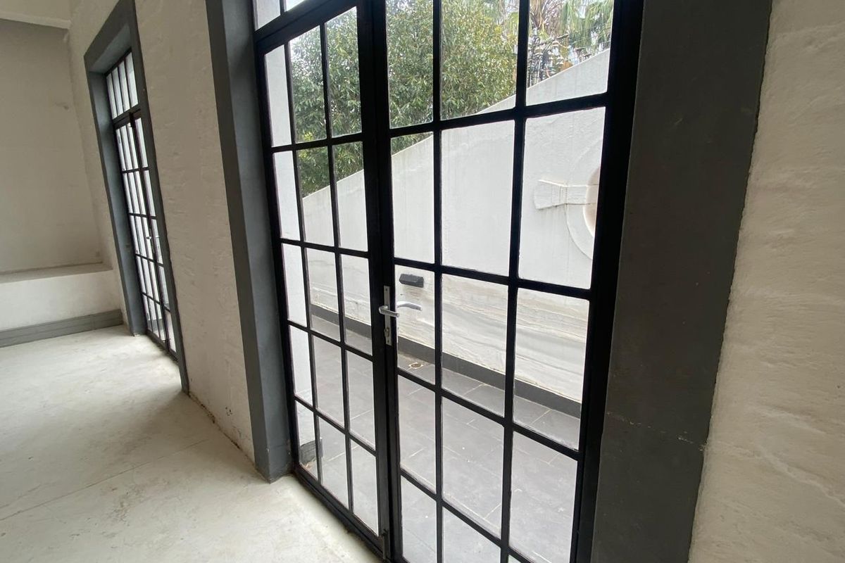 Bright interior space featuring industrial-style black-framed glass double doors leading to an outdoor patio area.
