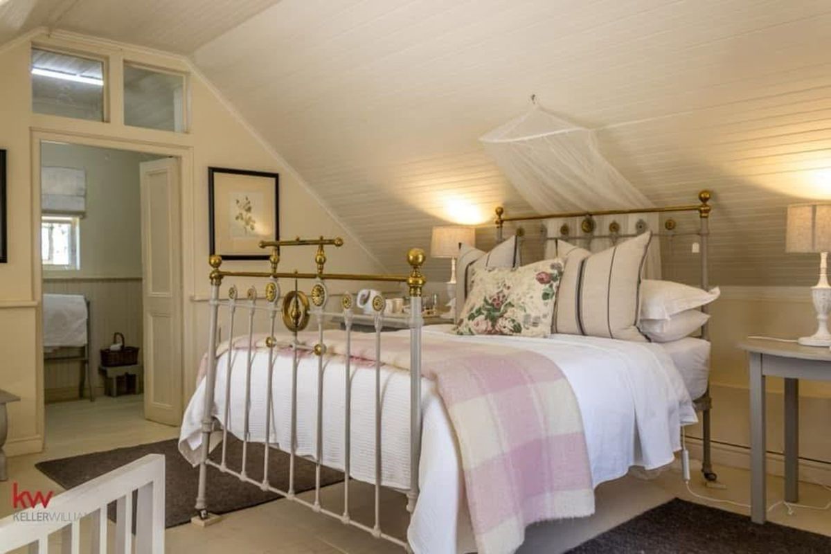 A cozy attic bedroom featuring sloped timber-paneled ceilings, neutral finishes, and an adjoining bathroom entrance.