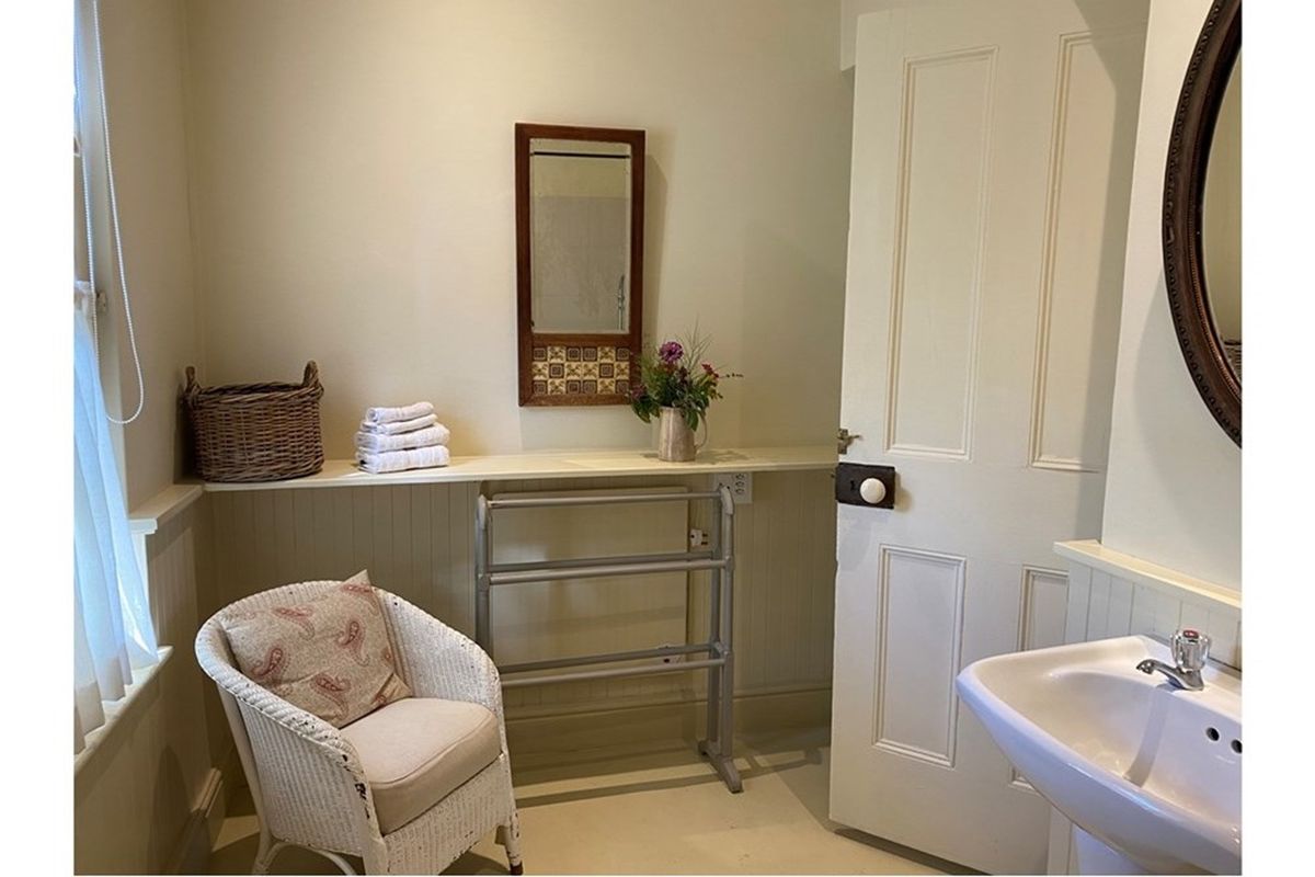 A functional bathroom featuring a wall-mounted basin, beadboard wainscoting, and a built-in shelf.