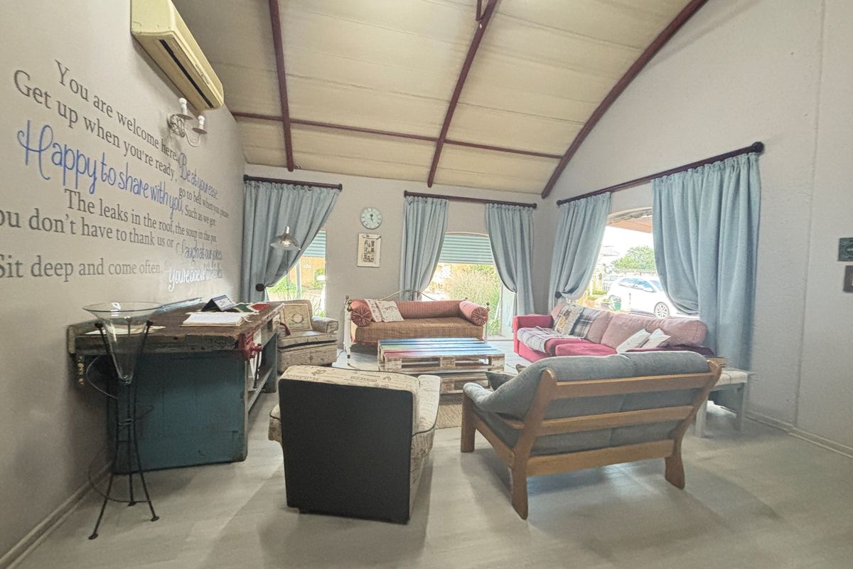 Spacious living room featuring high vaulted ceilings with exposed beams, tiled flooring, and large windows allowing for natural light.