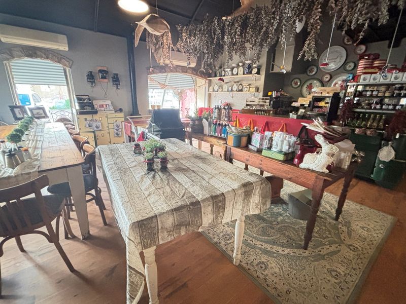 A rustic open-plan dining and retail area featuring exposed timber flooring, high ceilings, and integrated service counters within a guest house setting.