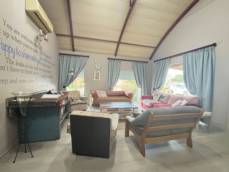 Spacious living room featuring high vaulted ceilings with exposed beams, tiled flooring, and large windows allowing for natural light.