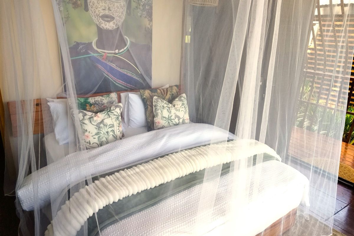 A cozy bedroom featuring timber flooring and a sliding glass door leading to an outdoor area, complete with a mosquito net canopy.
