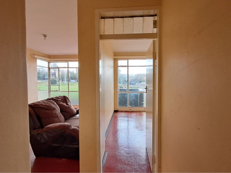 A view through a hallway connecting to a living area, featuring large windows and tiled flooring in need of cosmetic updates.