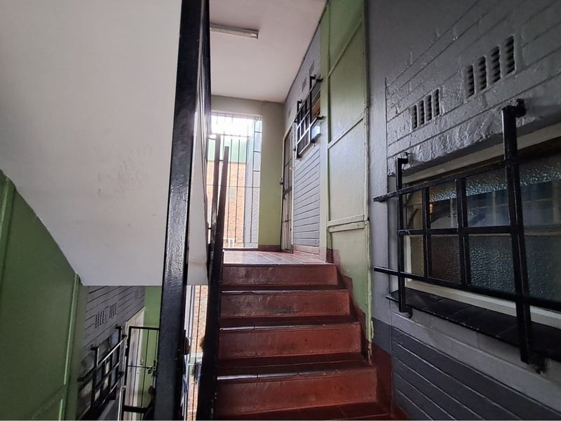 A functional stairwell and hallway area featuring painted brick walls, tiled stairs, and integrated security gates for building access.
