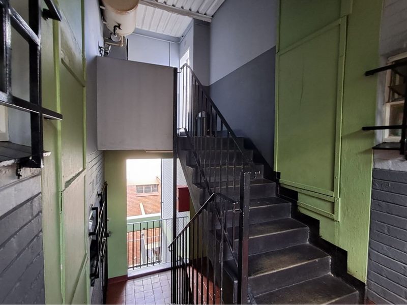 A functional stairwell area featuring metal stairs, handrails, and tiled flooring, showing signs of wear and dated paint finishes.
