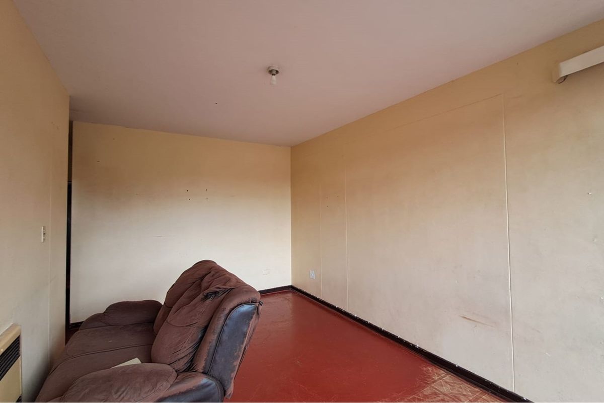 A sparsely furnished living area featuring painted concrete flooring and plain wall finishes, requiring cosmetic updates to improve the overall aesthetic.