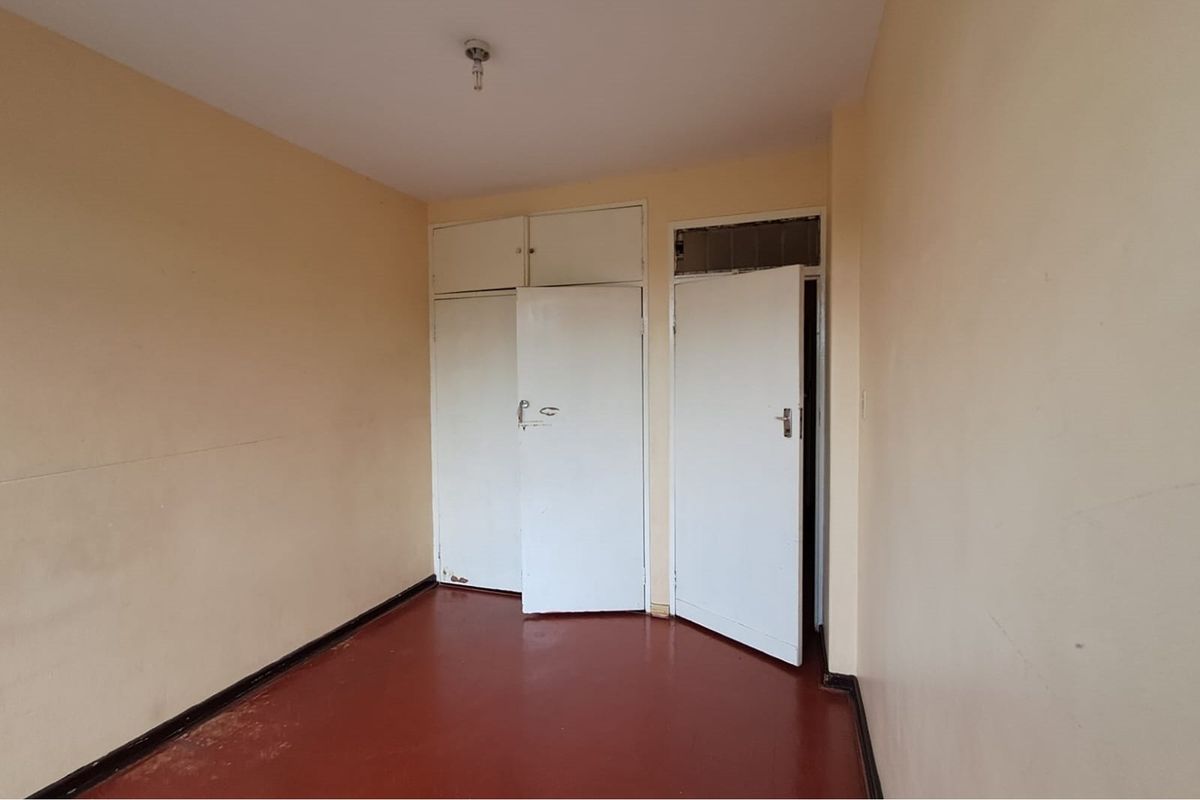 An empty bedroom featuring built-in cupboards with overhead storage, painted walls, and a solid floor finish.