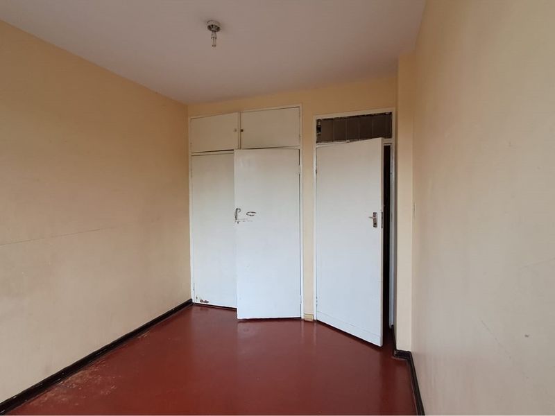 An empty bedroom featuring built-in cupboards with overhead storage, painted walls, and a solid floor finish.