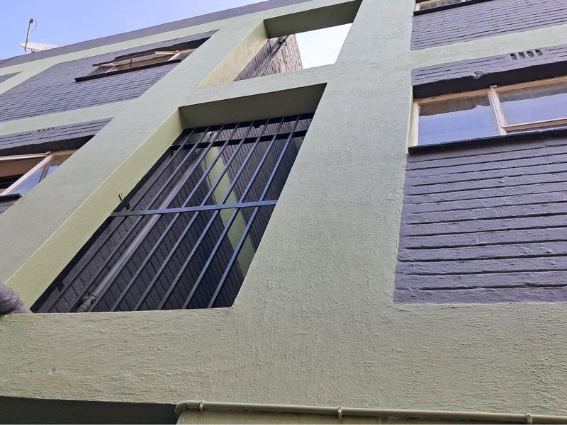 Low angle view of a multi-story retail building exterior featuring painted brickwork, security bars on windows, and external plumbing infrastructure.