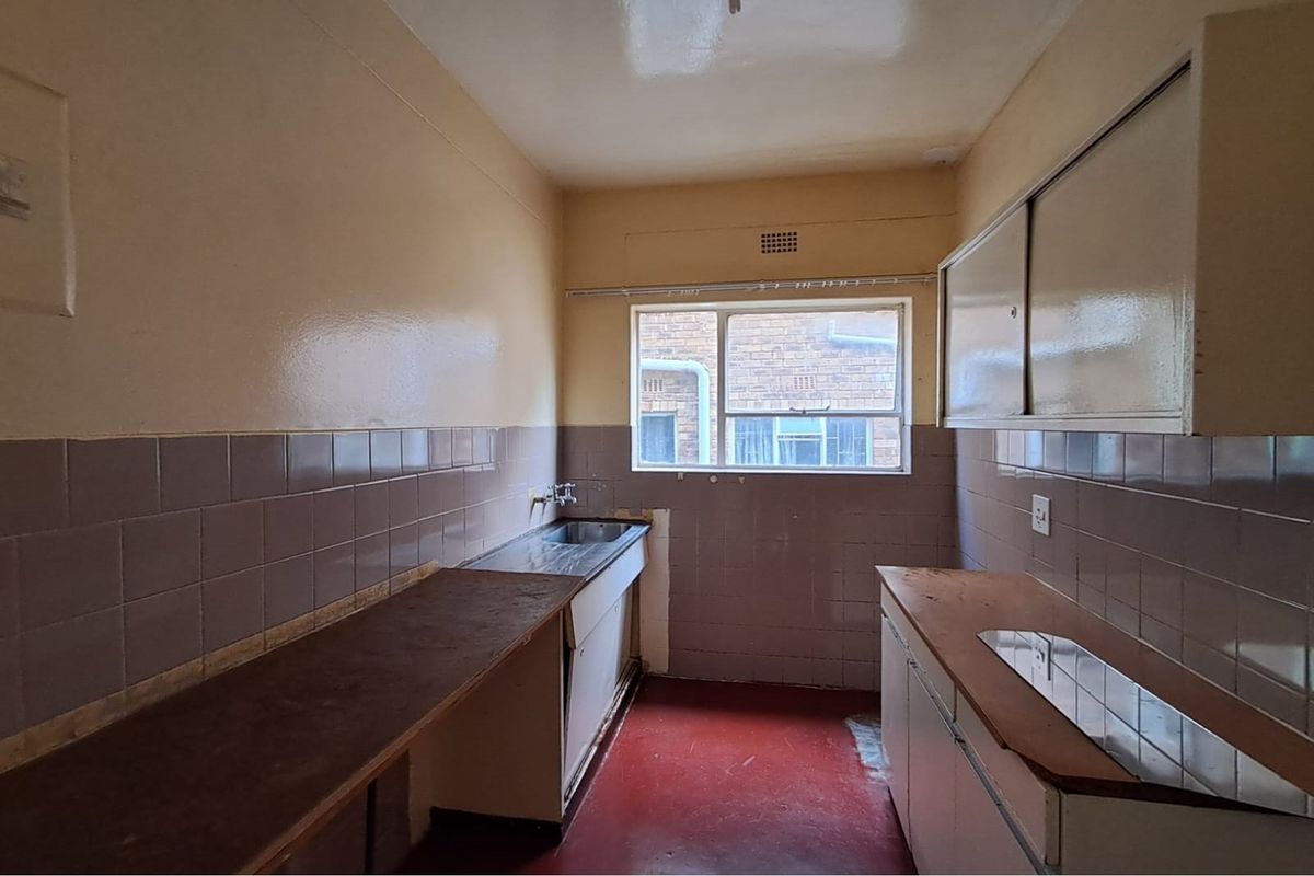 A dated, empty kitchen featuring built-in cabinetry, laminate countertops, a stainless steel sink, and tiled splashbacks, offering significant potential for renovation.