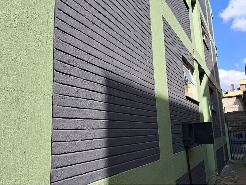 Side elevation of a multi-story retail building featuring a two-tone painted brick facade and casement windows.
