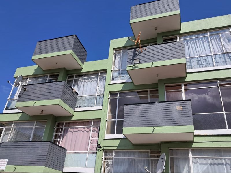 Exterior view of a multi-story building featuring multiple balconies, large windows, and a painted brick facade.