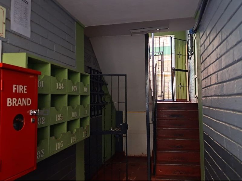 A functional building hallway featuring a fire hose reel, wall-mounted mailboxes, and a staircase leading to an exterior security gate.