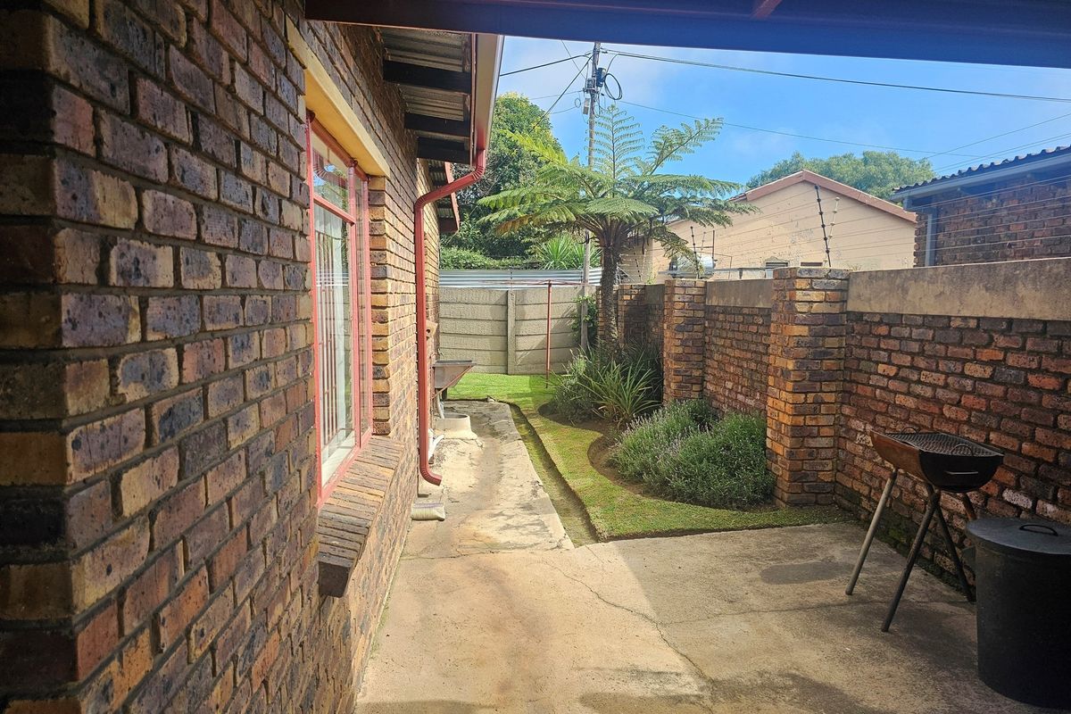 A side exterior view featuring a brick facade, concrete pathway, and a small landscaped garden area enclosed by a brick boundary wall.