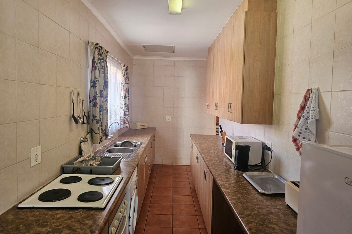 A functional galley-style kitchen featuring laminate countertops, built-in cabinetry, a four-plate electric hob, and a stainless steel sink.