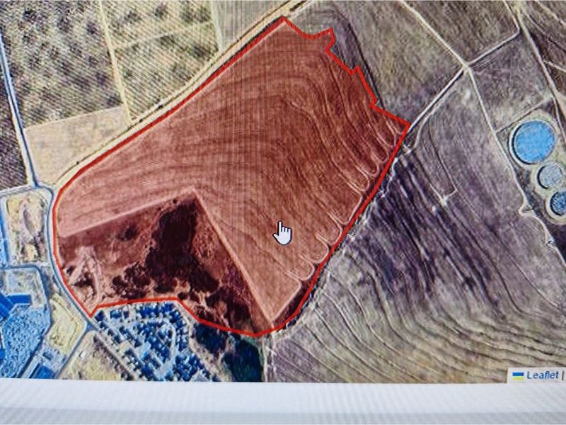 Aerial view of a large commercial land parcel with red boundary outline, showing surrounding terrain and nearby infrastructure.