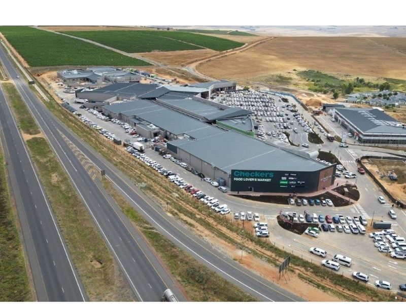 Aerial view of a large commercial shopping center featuring extensive parking facilities and direct highway access in a suburban setting.