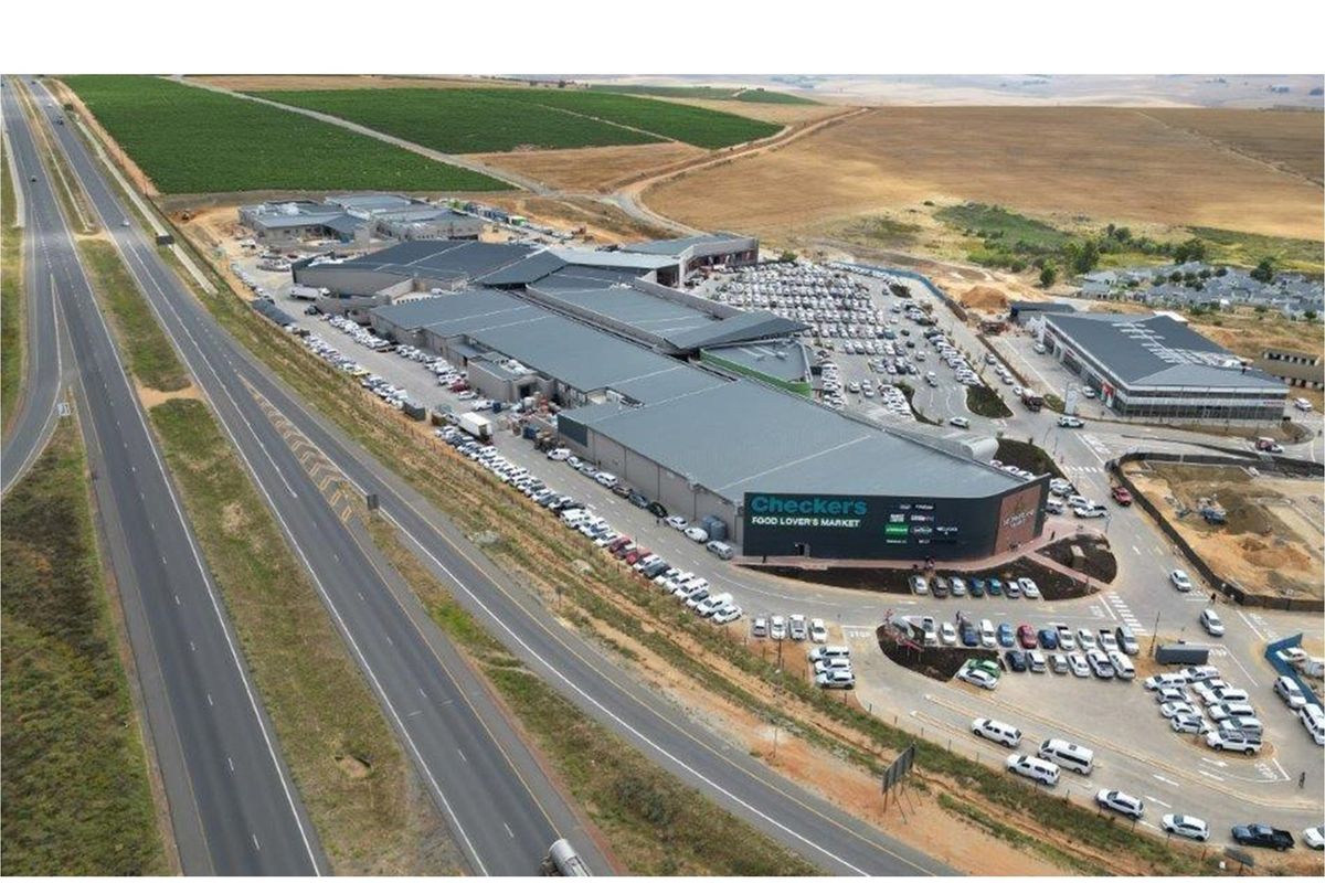 Aerial view of a large commercial shopping center featuring extensive parking facilities and direct highway access in a suburban setting.